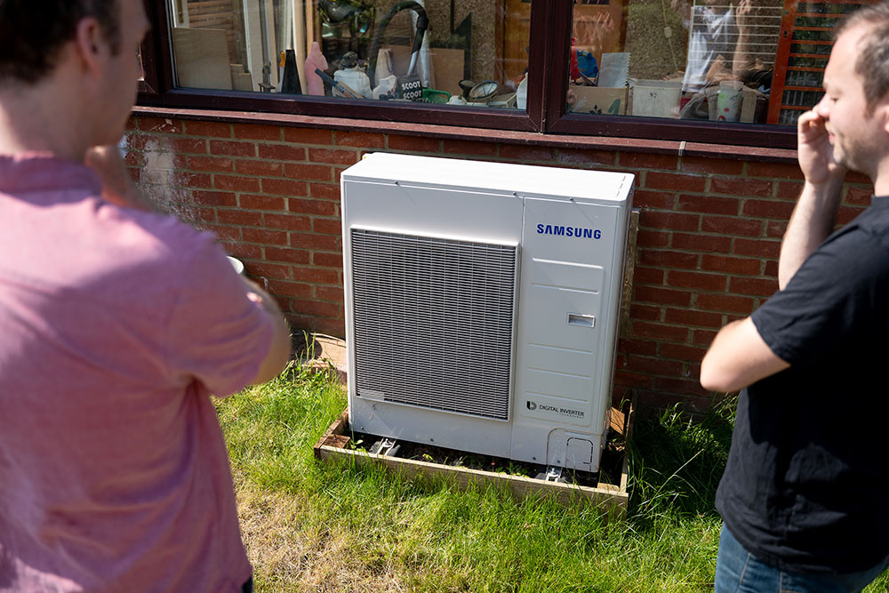 Heat pump owner demonstrates it to a visitor outside their home